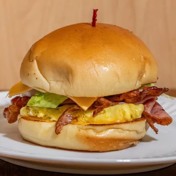 JJ Cafe's breakfast sandwich with scrambled eggs, bacon, ham, cheese, and lettuce on a bun.