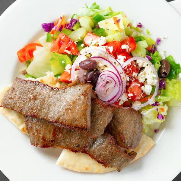 JJ Cafe's breakfast gyro with sliced meat, fresh salad, feta, red onion, and olives on pita bread.