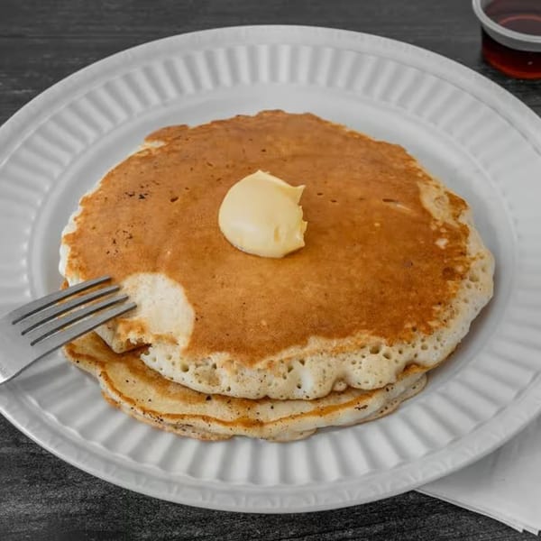 Fluffy pancakes with a pat of butter and a fork on a white plate at JJ Cafe.