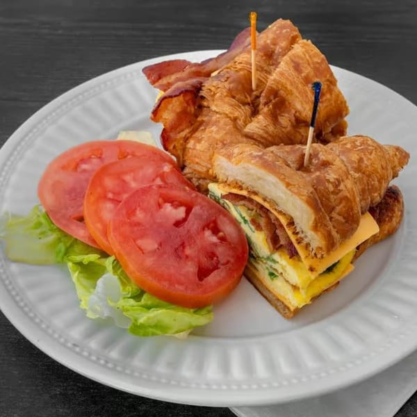 JJ Cafe's breakfast croissant sandwich with bacon, egg, cheese, and a side of lettuce and tomato.