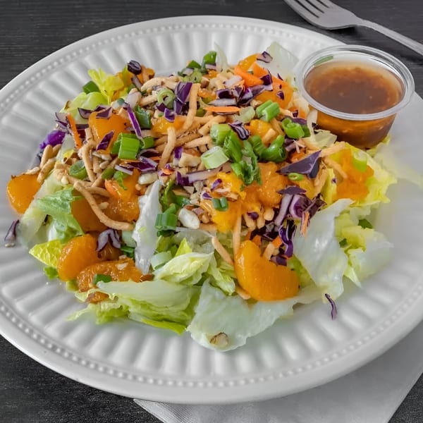 A vibrant Asian chicken salad with mandarins, cabbage, and crispy noodles on a white plate.